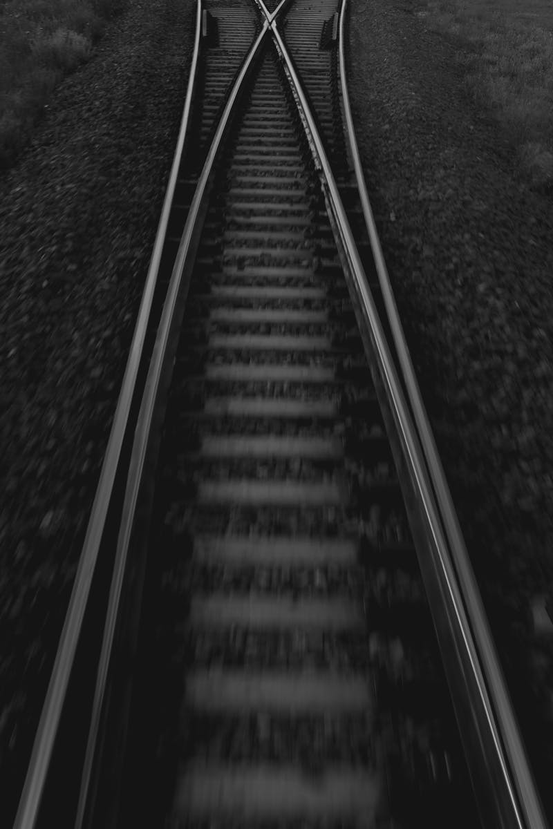 Artistic black and white photograph of intersecting railway tracks captured from a high angle, creating a dramatic and nostalgic effect.
