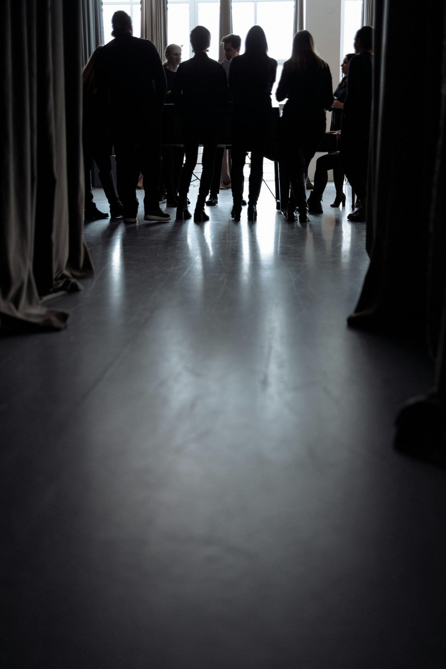 Silhouetted group of people gathering in a dimly lit room with curtain shadows and windows.